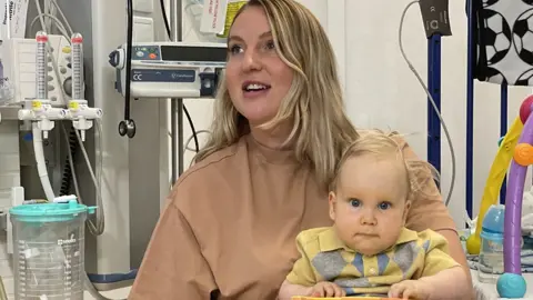 Megan holds baby Edward on her lap, in a hospital room.