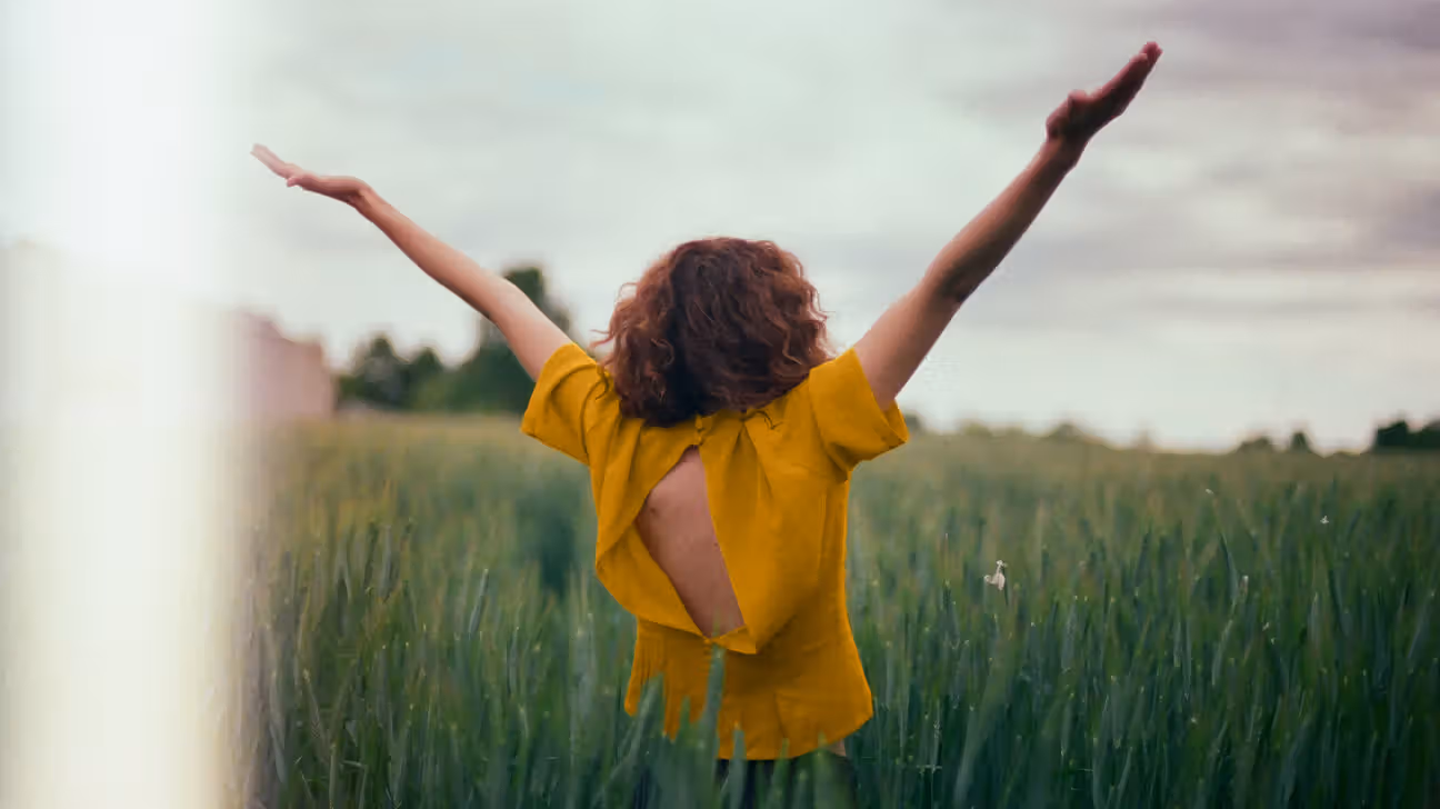 Female in a field with her arms in the air as though she is happy