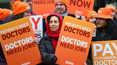 Getty Images Participants hold placards outside Bristol Royal Infirmary hospital on the first day of a five day resident doctors strike, on December 17, 2025 in Bristol, England. 