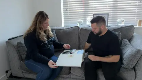 BBC Shane Bevan and Laura Tongue looking through a memory box after the death of their son. They are sitting ona grey sofa in their home