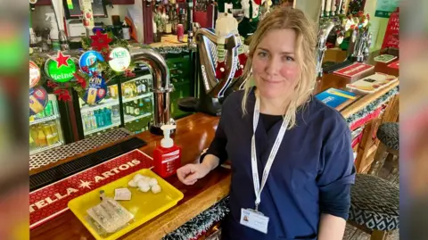 Mark Norman/BBC A nurse stands at the bar of a pub with flu vaccination equipment. 