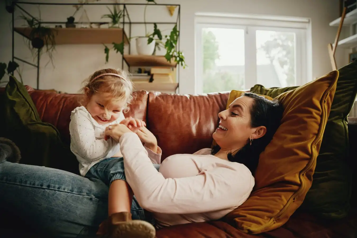Cheerful mother and daughter tickling and playing at home on couch