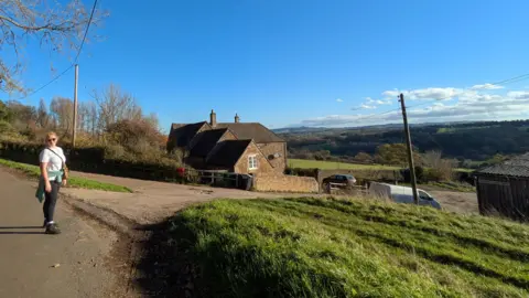 Cathy Read Woman in sunglasses smiling in a countryside setting with rolling fields and farm houses