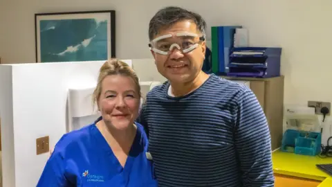 PA Media A man wearing goggles, looking at the camera. He is standing next to a female medic with blonde hair tied back. Both smiling. 