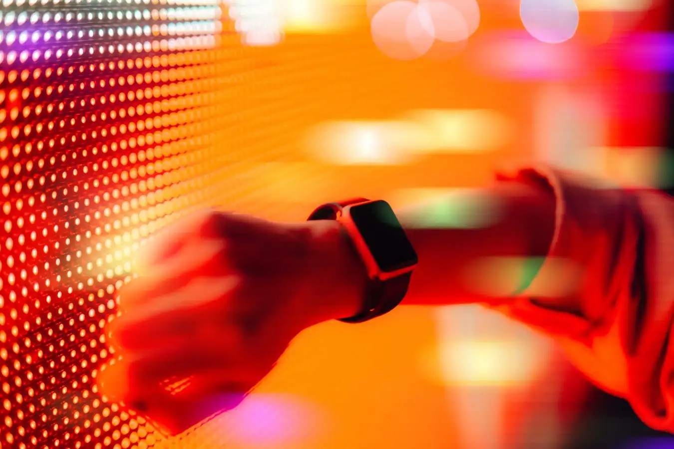 Close up shot of a woman using smart watch against colourful neon light display