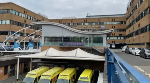 Outside the QMC - a large brown building with four ambulances in front of it.