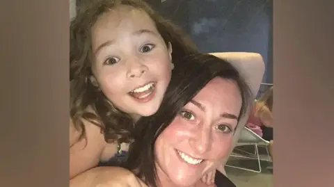 Kimberly Darroch Milly Main smiling while looking at the camera. She has long brown hair. She is on the back of Kimberly Darroch, who has long black hair and is also smiling at the camera.