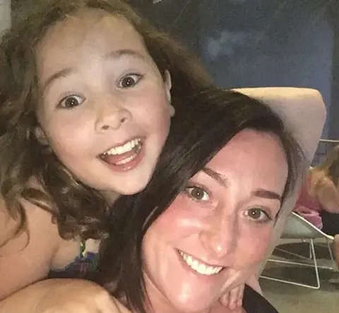 Kimberly Darroch Milly Main smiling while looking at the camera. She has long brown hair. She is on the back of Kimberly Darroch, who has long black hair and is also smiling at the came