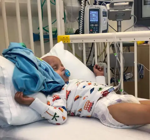 Karen Stirrat A young child in a hospital bed. He is hooked up to various lines and there is medica equipment in the background