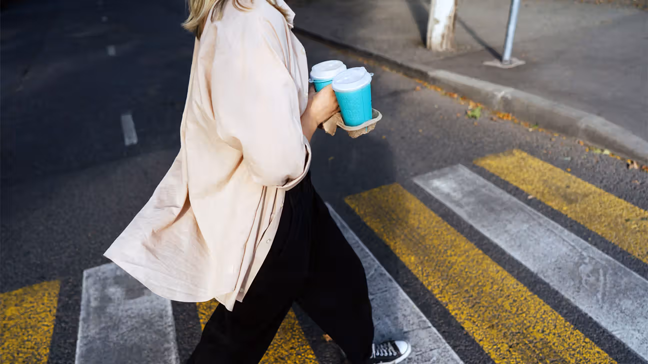 Female carrying paper to-go coffee cups while crossing the road