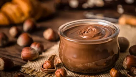 Getty Images A jar of chocolate and hazelnut spread surrounded by hazelnuts