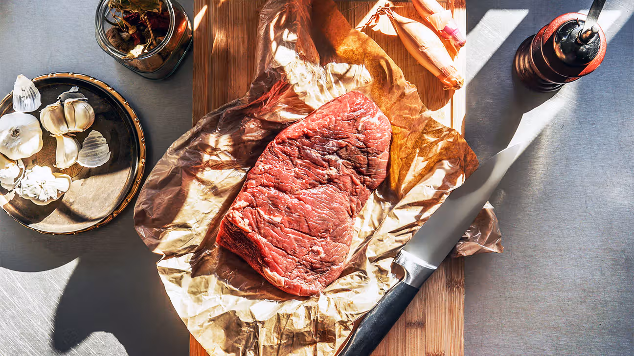 Raw steak sitting on butcher's paper on a counter with other cooking ingredients
