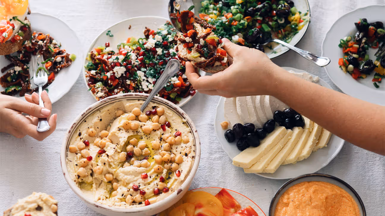 People sharing food at a table, including hummus and vegetables