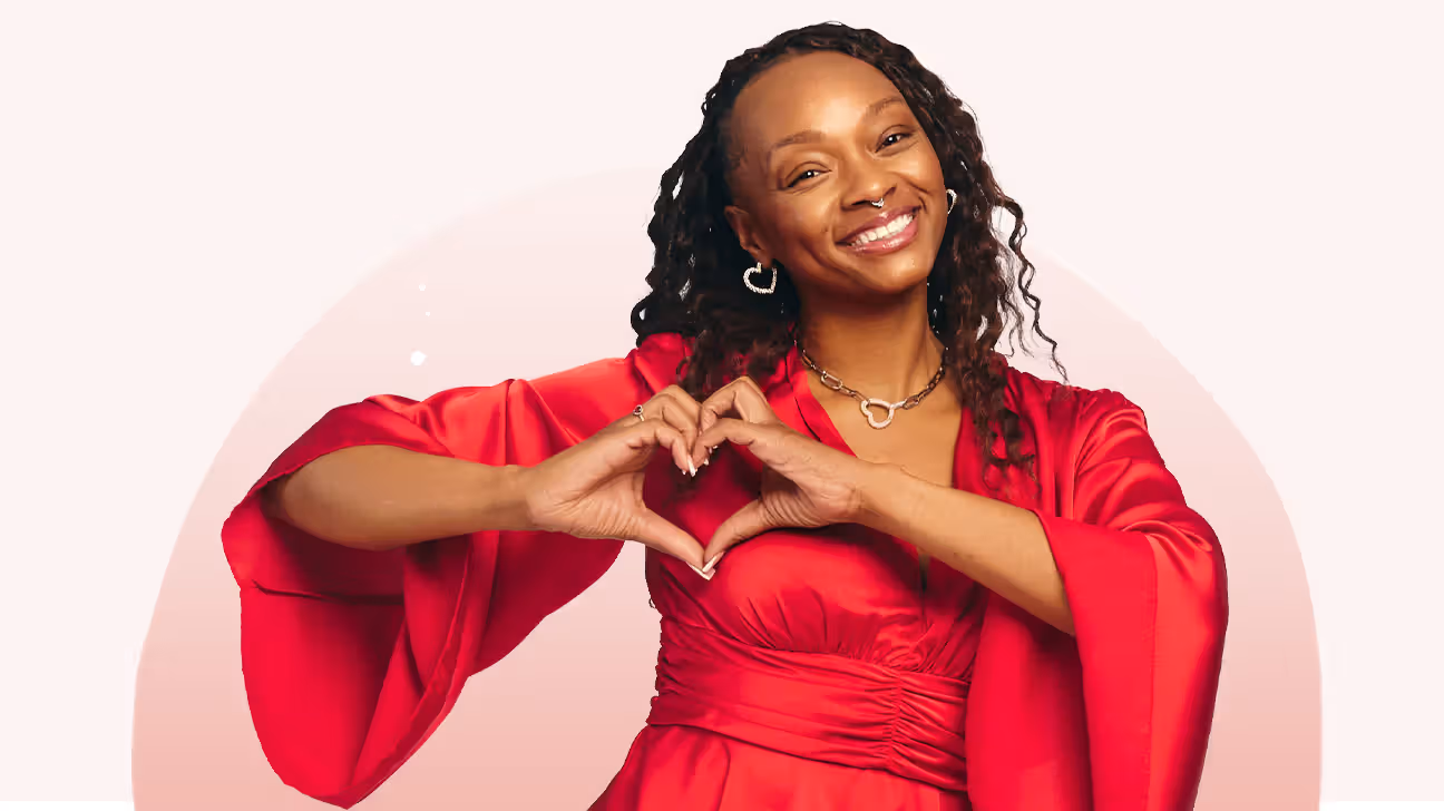 Angellica in a red dress, smiling and making a heart symbol with her hands
