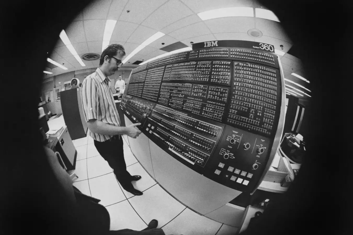 Fish eye lens view of a man, wearing a striped short-sleeve shirt, inspecting an IBM System/360 Model 91 mainframe computer system, United States, circa 1965. (Photo by Dwight Ellefsen/FPG/Archive Photos/Getty Images)