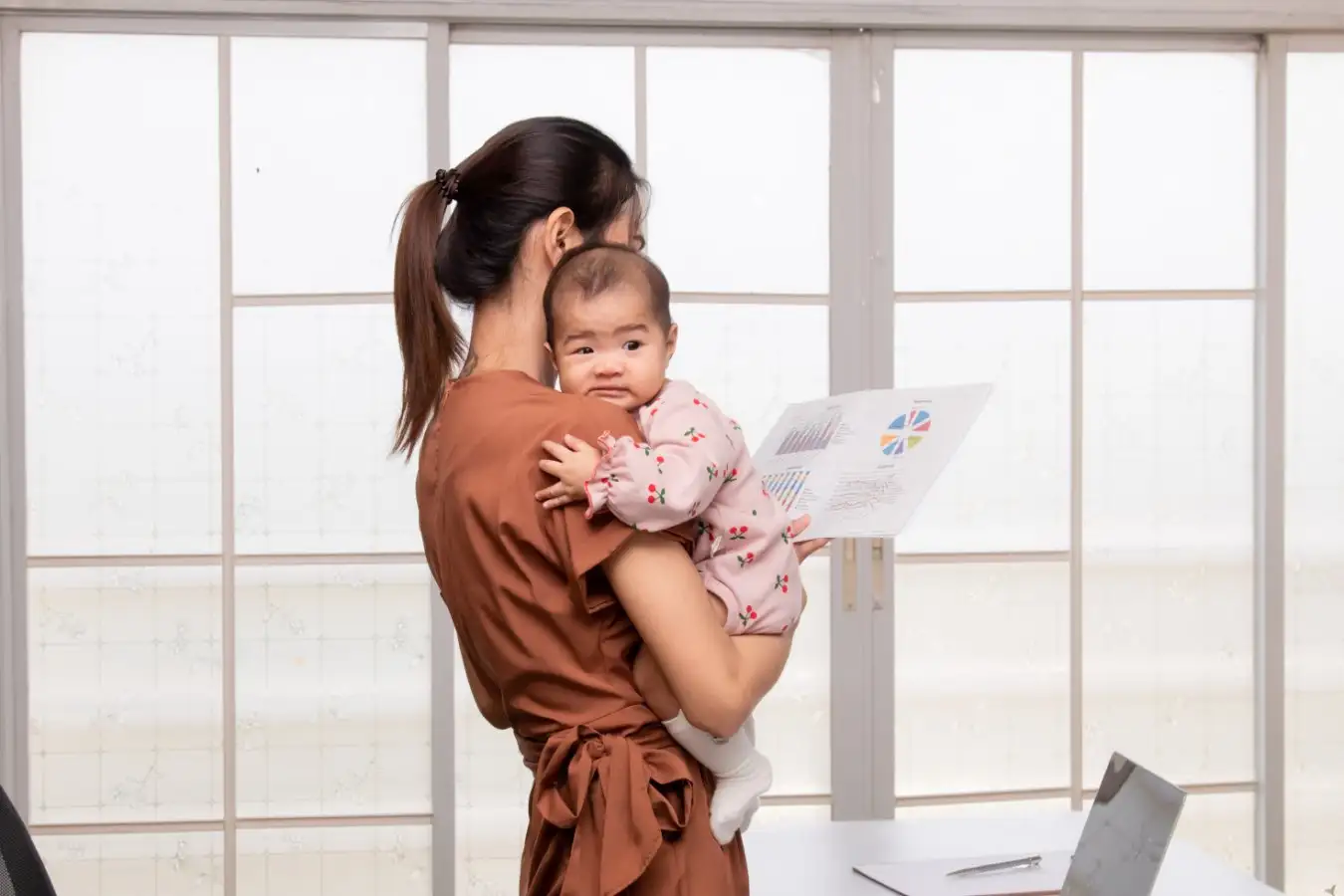 Asian single mother holding newborn baby while working from home