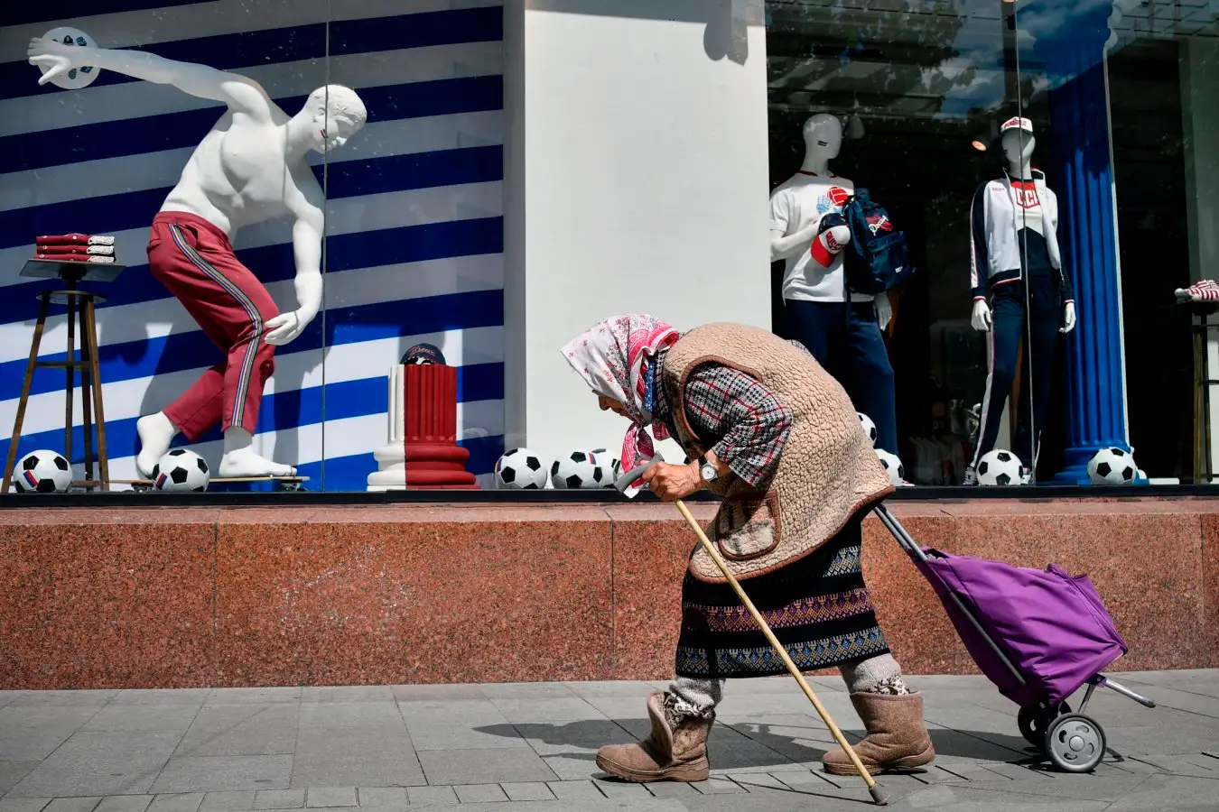 An elderly woman walks past a sports shop. 