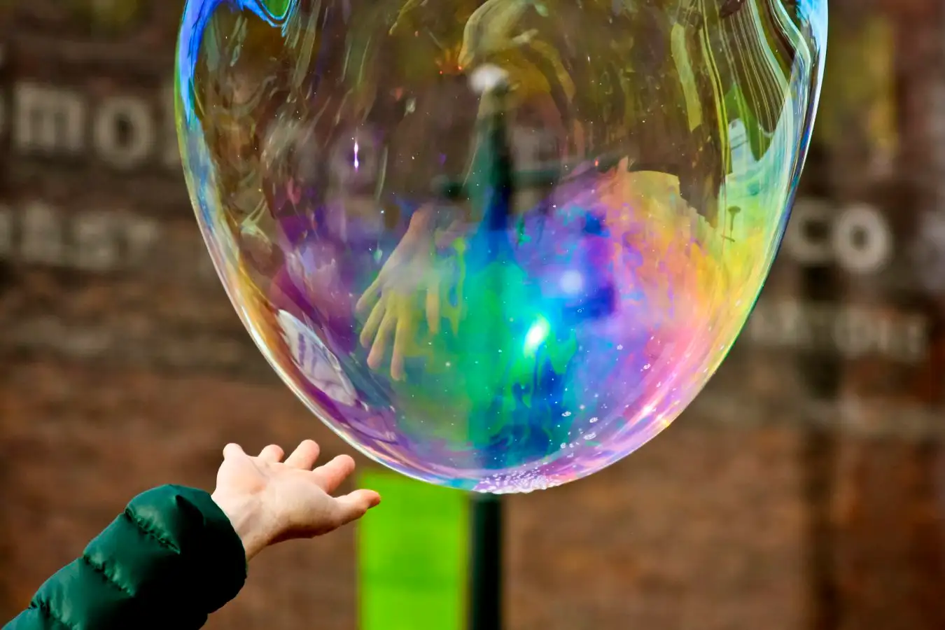 A child's hand reaching towards a huge soap bubble, about to pop it.