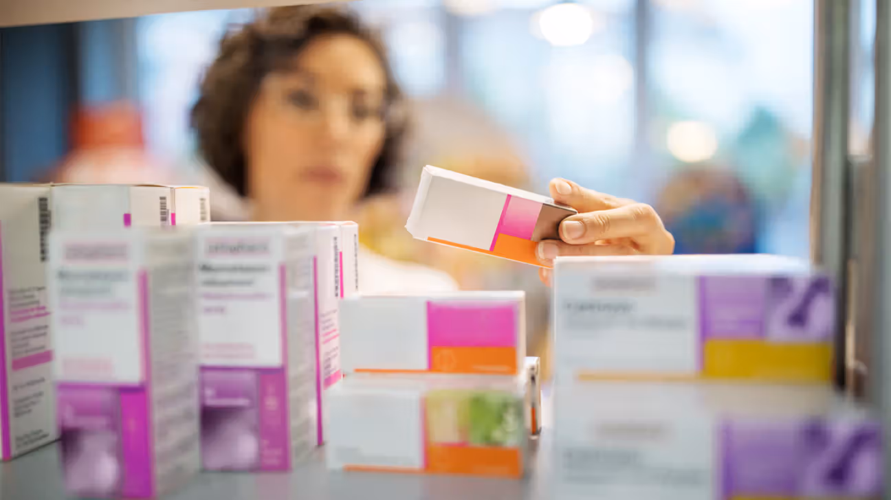 A pharmacist examining boxes of medication on a shelf.