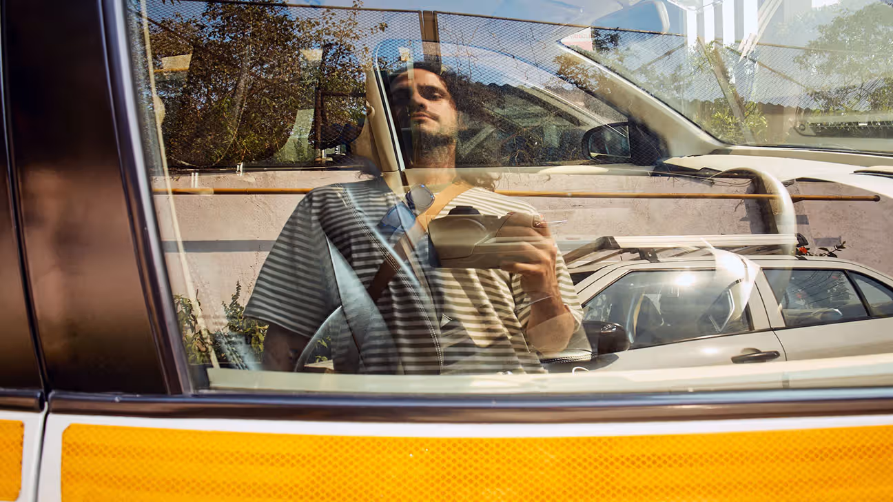 A man looking at his reflection in a car window.