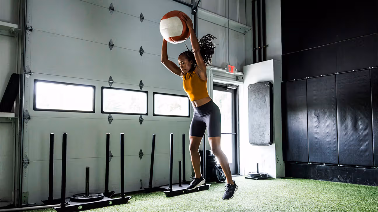 Female jumping up to catch a large ball in a gym setting