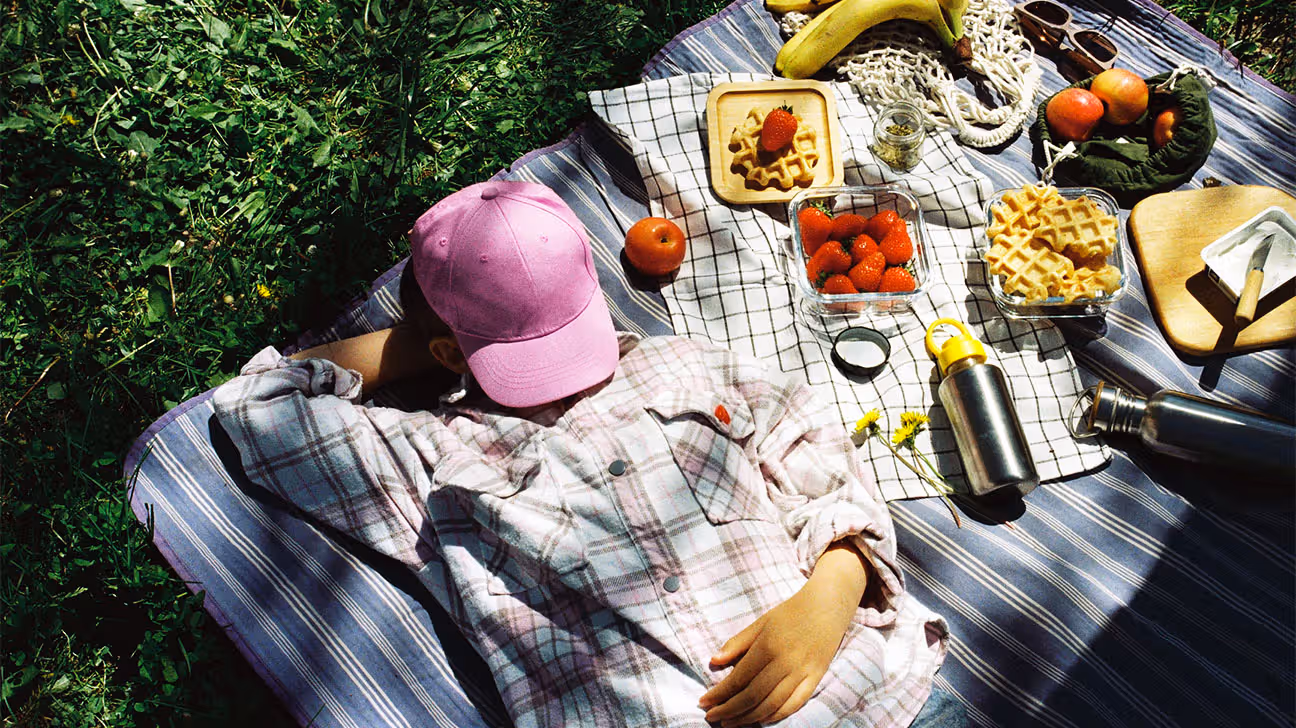 Female lying on a picnic blanket in the shade with a pink hat covering her face