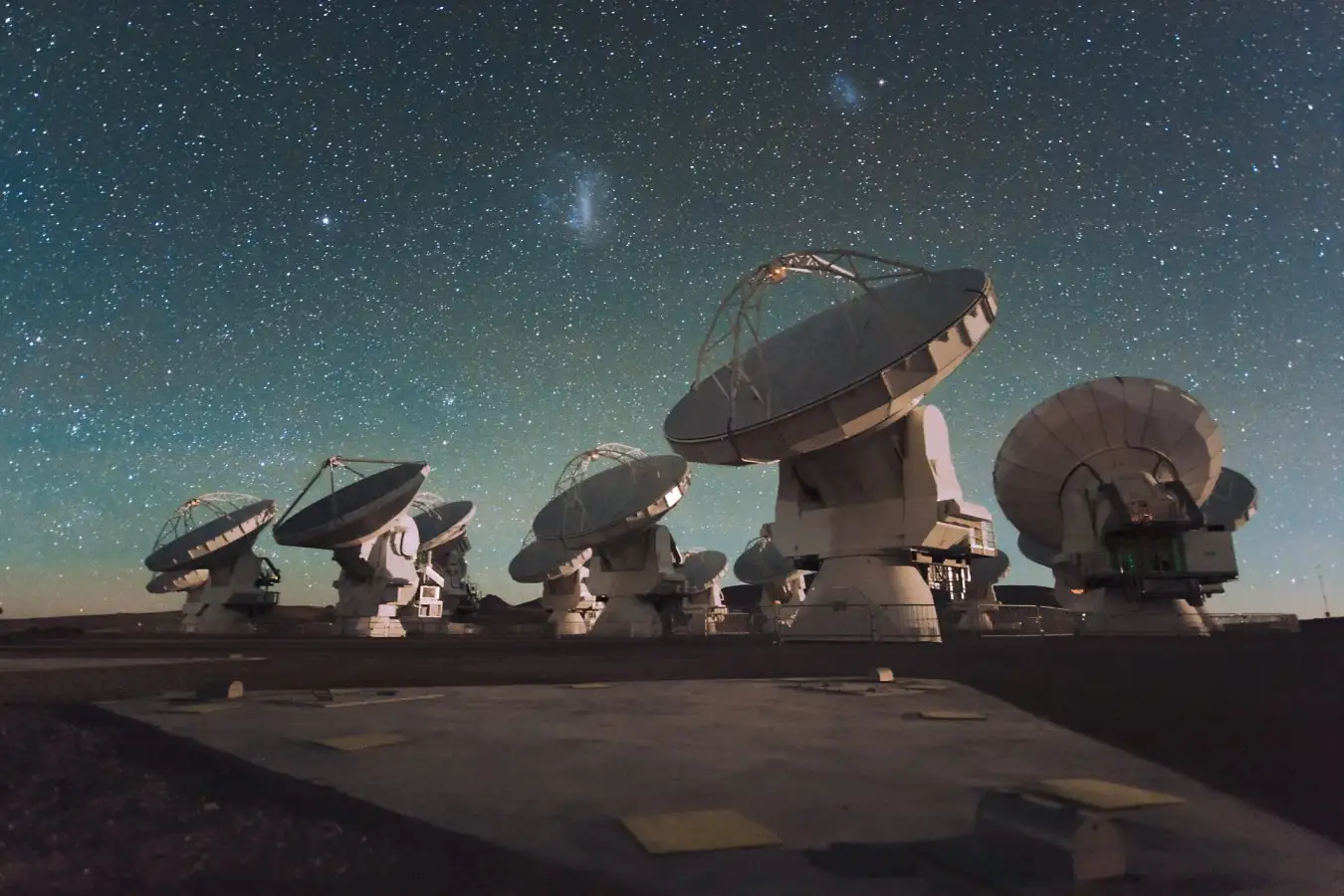 Antennas of the Atacama Large Millimeter/submillimeter Array (ALMA), on the Chajnantor Plateau in the Chilean Andes. The Large and Small Magellanic Clouds, two companion galaxies to our own Milky Way galaxy, can be seen as bright smudges in the night sky, in the centre of the photograph.