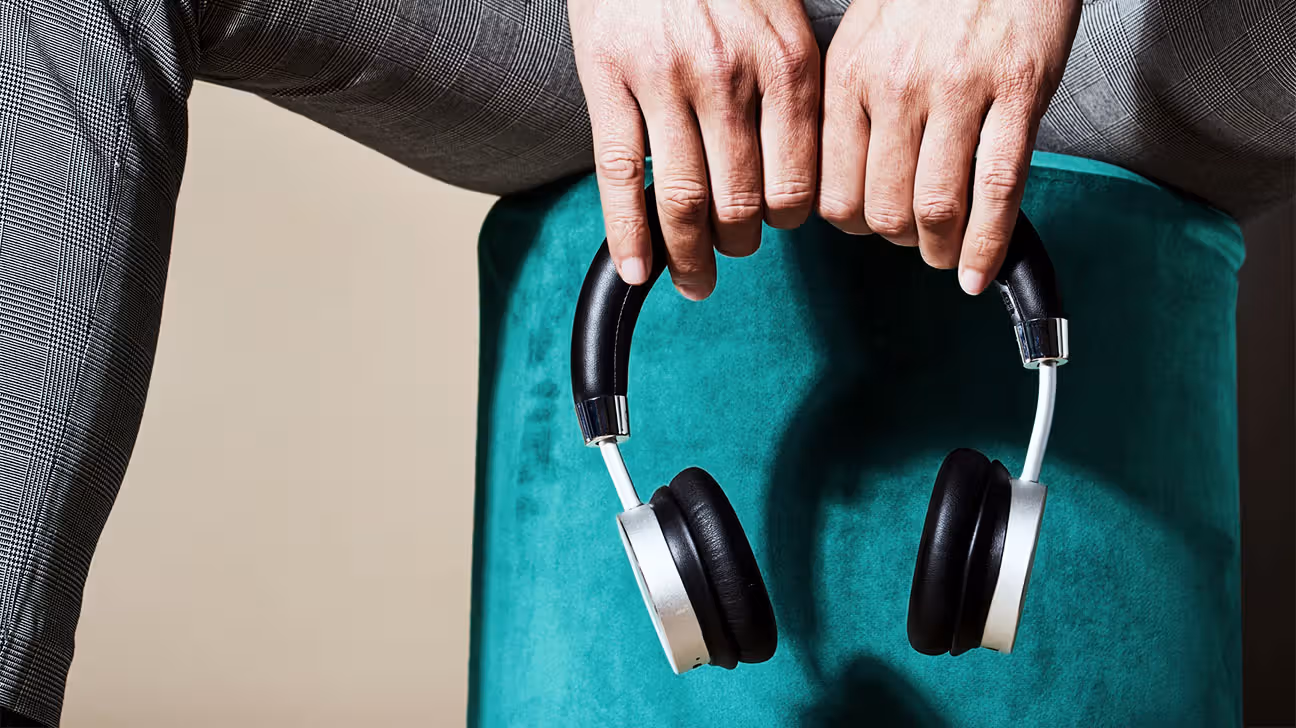 Person holding a pair of headphones against a teal background