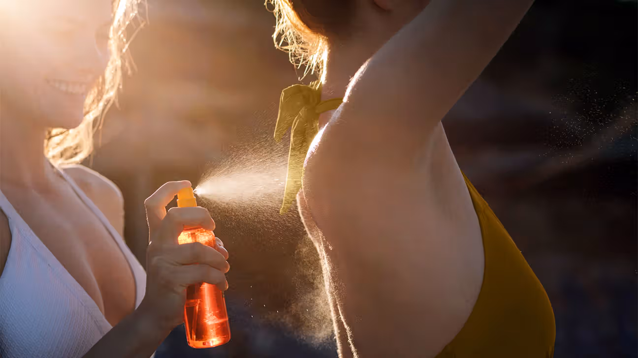 A female spraying sunscreen onto another female while outside in the sun