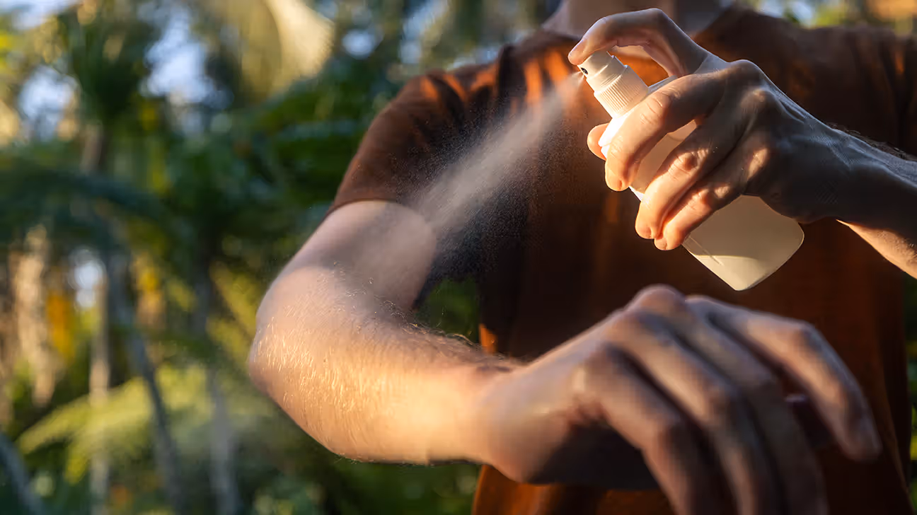 Male spraying DEET on arms