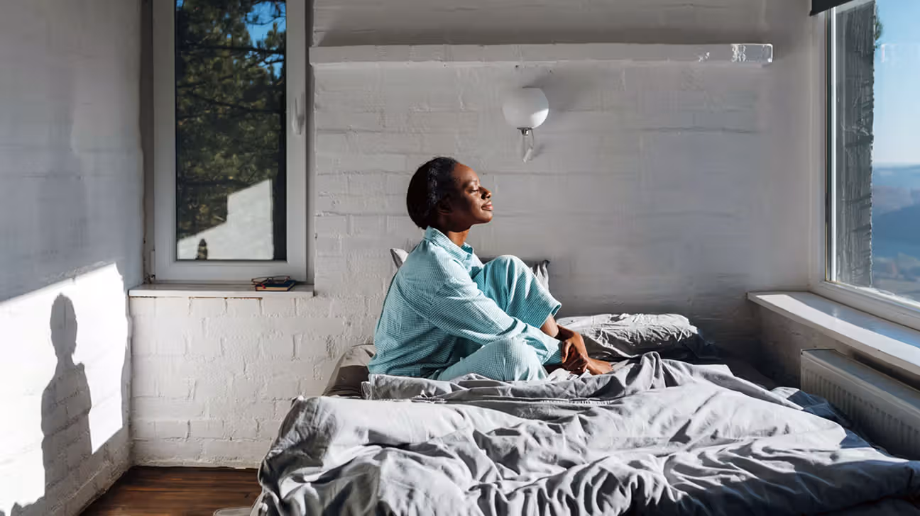Person sitting on their bed with sun shining on them through the window