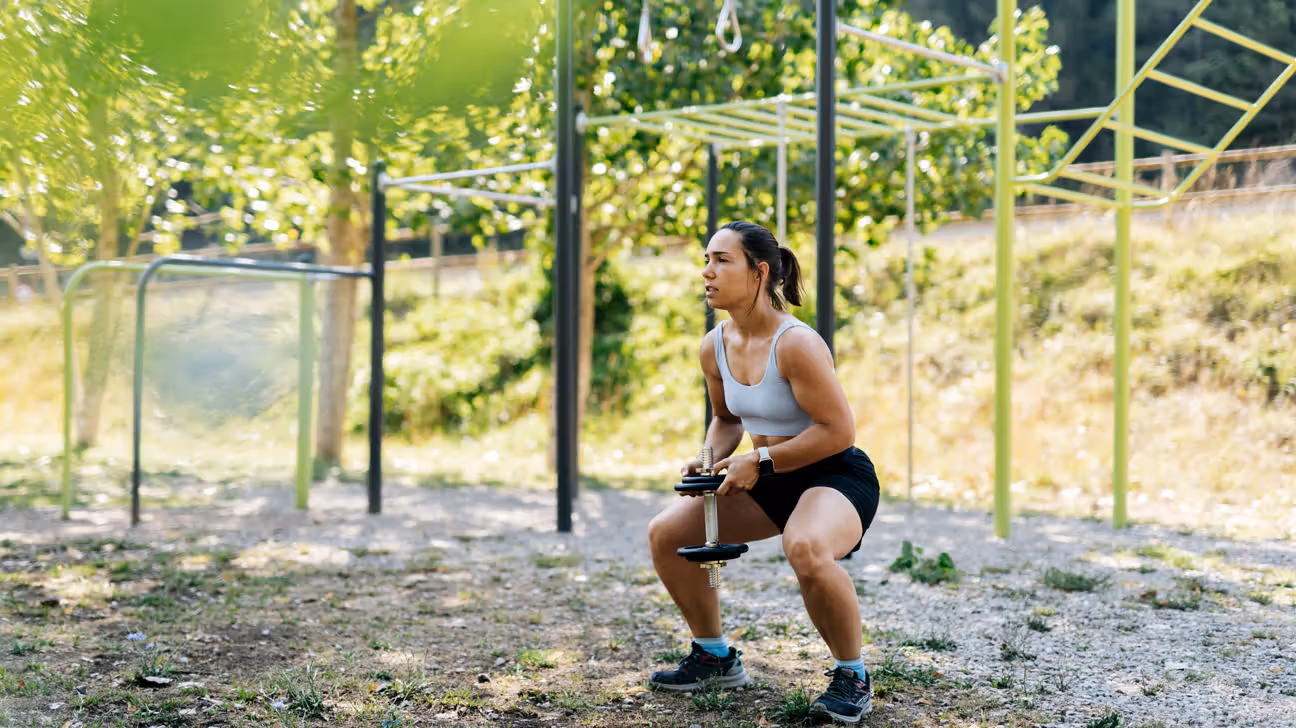 Female doing squats with a dumbbell in a park