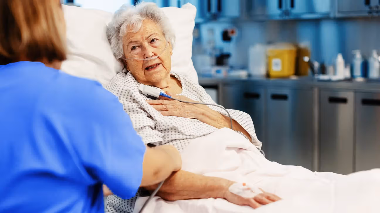 Older female patient in hospital bed talks with doctor