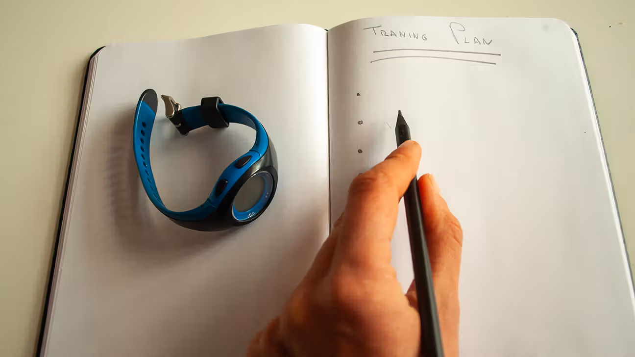 A person's hand writing in a journal with a fitness tracker next to them