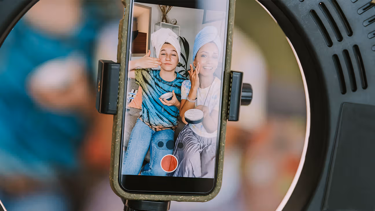 Two young females viewed through a phone screen recording a video