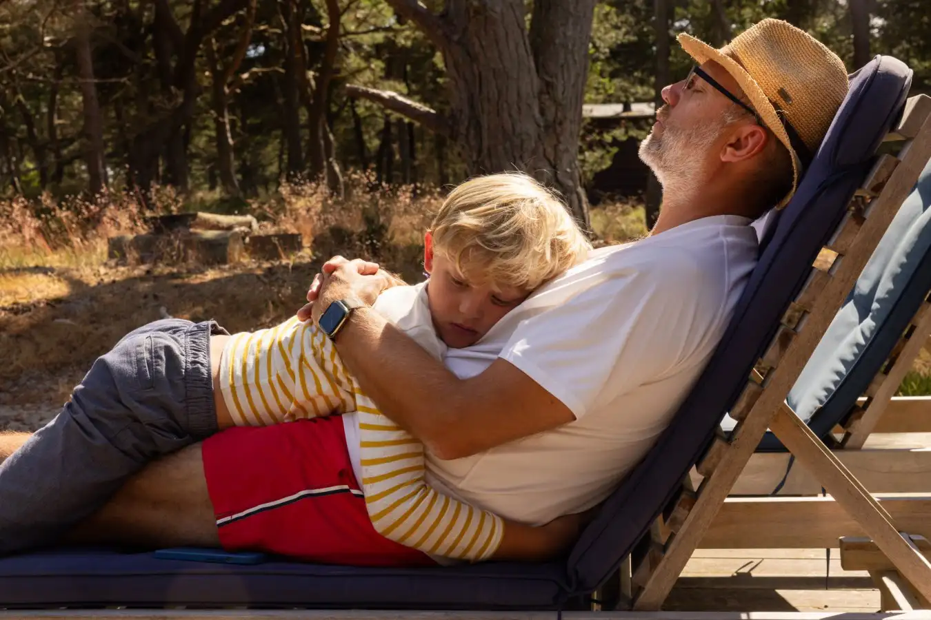 Son sleeps on his father's stomach in a deck chair