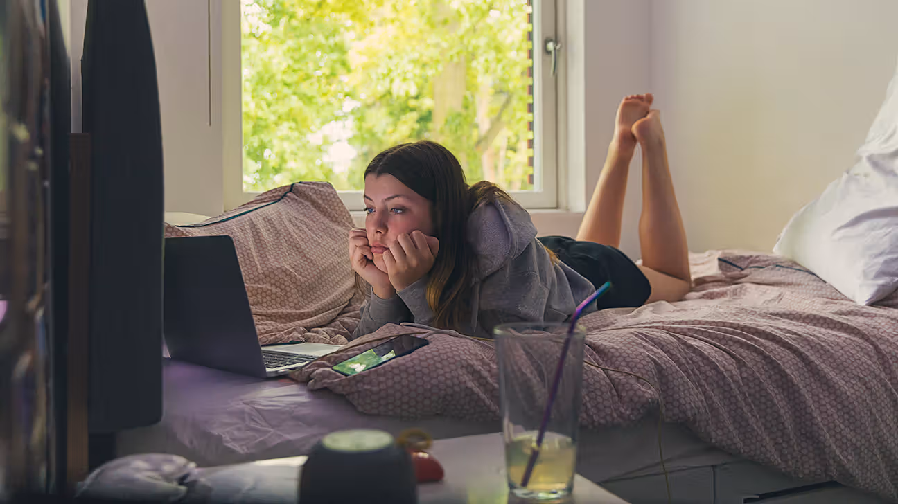 Teenaged female lying on her bed looking at a laptop