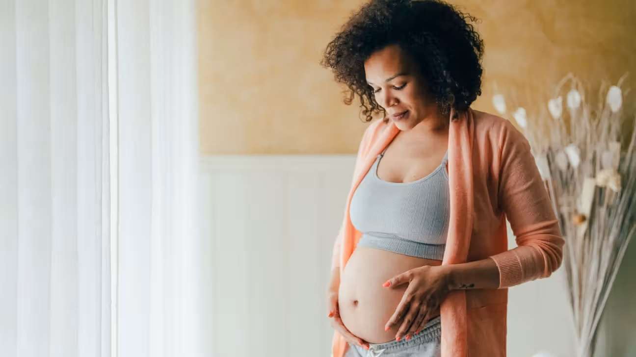Ethnic pregnant female caressing her belly and looking down at it