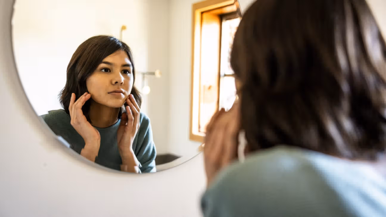 Younger female checking her skin in a mirror